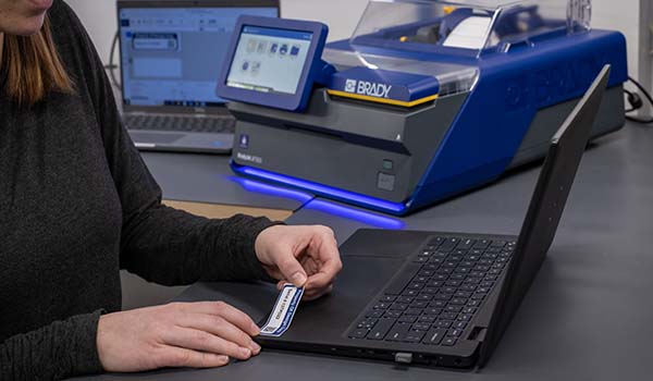 Egy dolgozó eszközcímkét helyez egy laptopra.