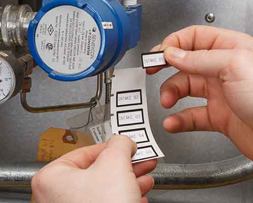 Egy személy M610-zel nyomtatott címkéket ragaszt egy gépre.